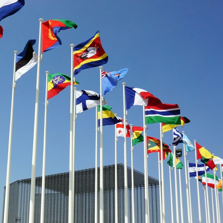 A row of various international flags against a clear blue sky.